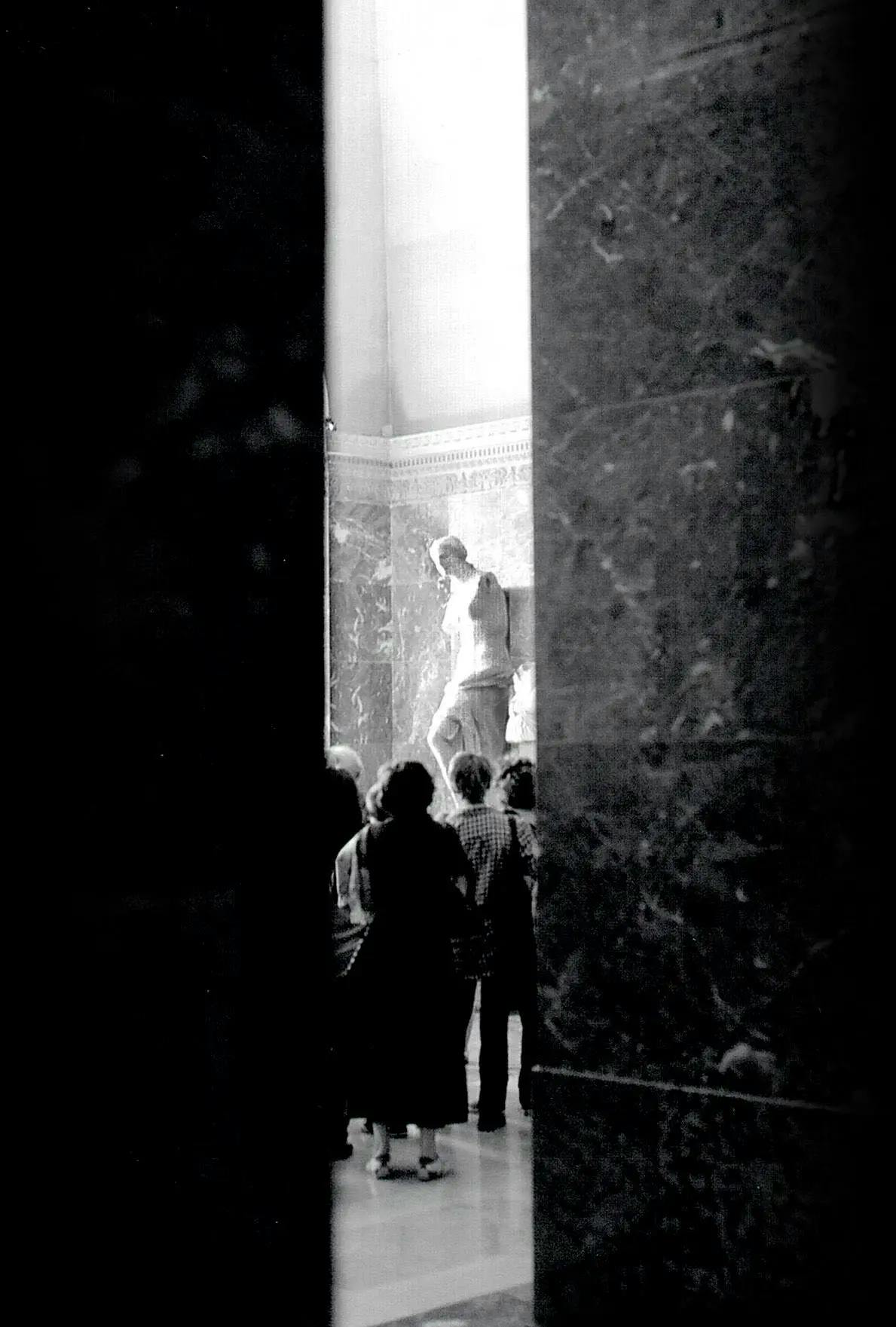 The white marble roman statue, Vinus de Milo, in the Louvres surrounded by a handful of onlookers.